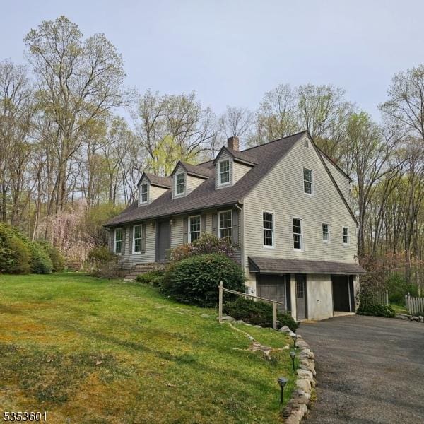 view of side of property with a garage, a chimney, a shingled roof, a lawn, and driveway