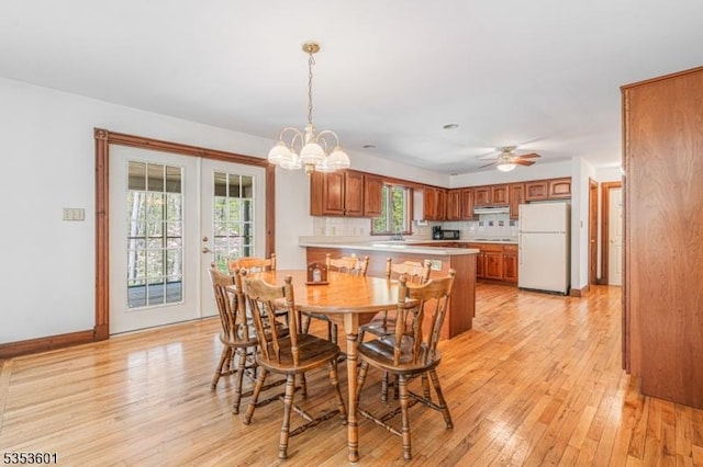 dining room featuring french doors, light wood finished floors, ceiling fan with notable chandelier, and baseboards