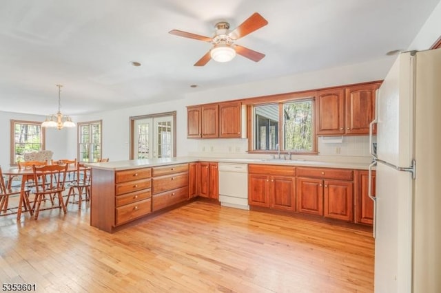kitchen with brown cabinetry, light countertops, a peninsula, light wood-style floors, and white appliances