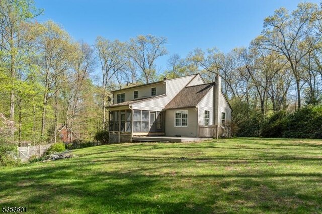 rear view of property featuring a lawn, a chimney, a sunroom, and a wooden deck