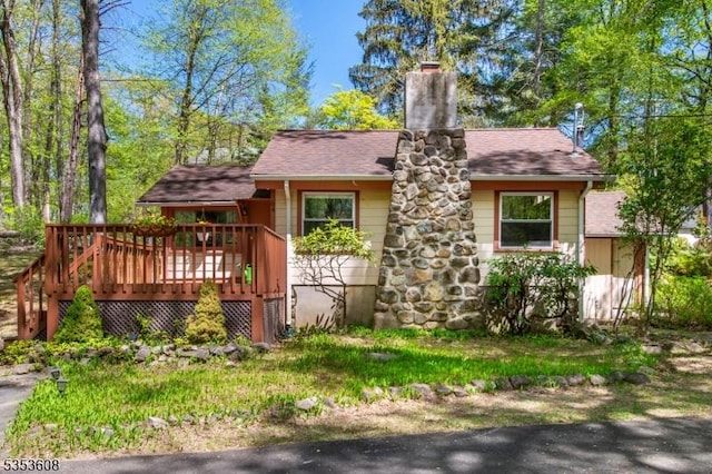 view of front of property with a deck, a chimney, and a shingled roof