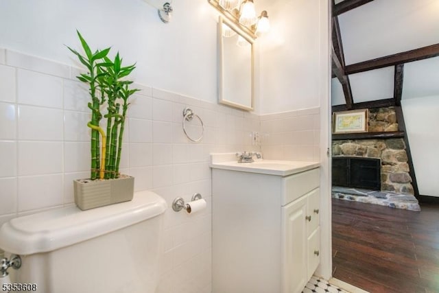 half bathroom with vanity, wood finished floors, toilet, tile walls, and a stone fireplace