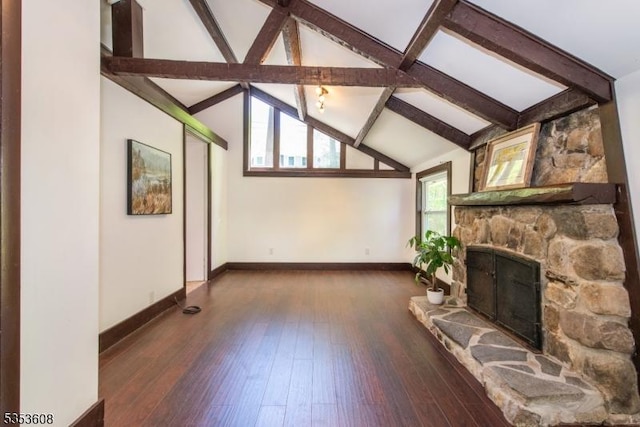 unfurnished living room featuring hardwood / wood-style floors, baseboards, lofted ceiling with beams, and a stone fireplace