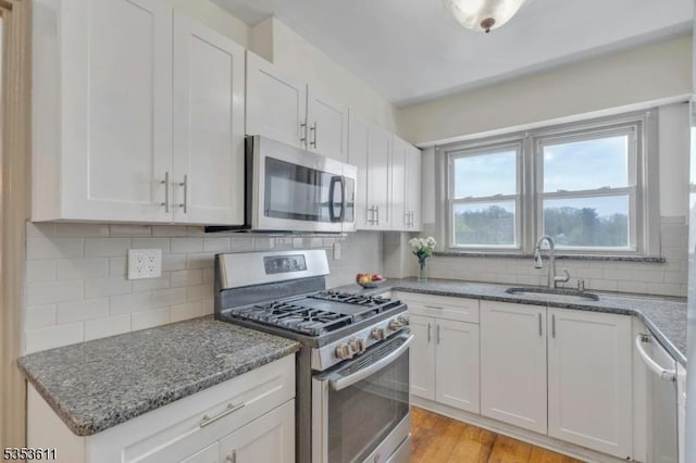 kitchen with backsplash, a sink, white cabinets, stone counters, and stainless steel appliances