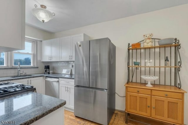 kitchen with decorative backsplash, dark stone counters, white cabinetry, a sink, and stainless steel appliances