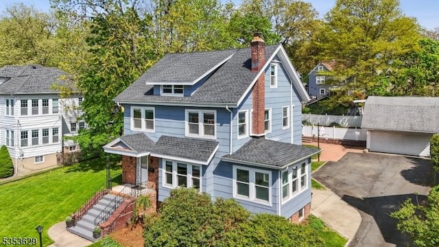 view of front facade featuring a shingled roof, a chimney, and a front lawn
