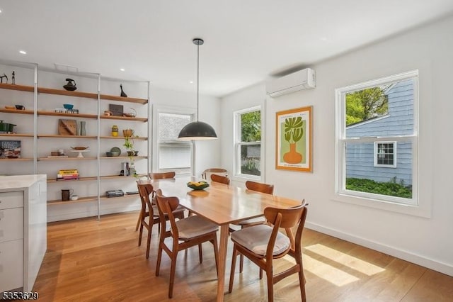 dining room featuring plenty of natural light, baseboards, light wood-style floors, and a wall unit AC