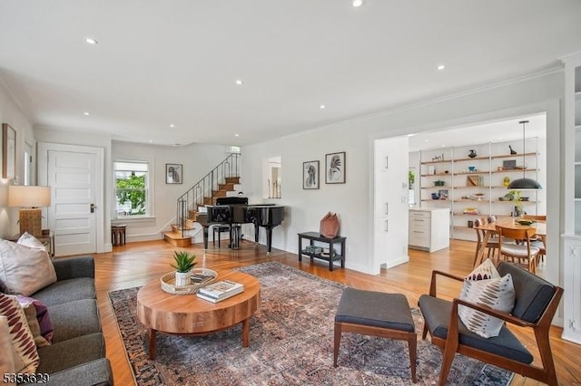 living area with light wood-style floors, crown molding, and stairs