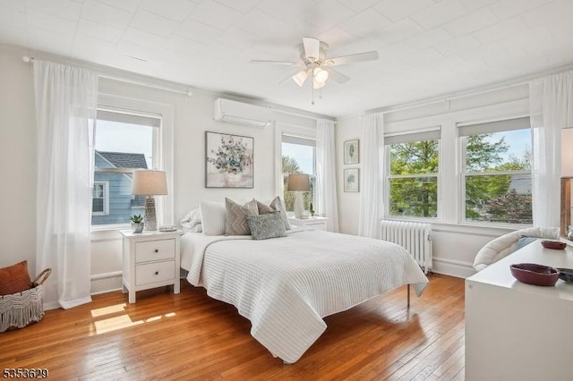 bedroom with light wood-type flooring, baseboards, a wall unit AC, and radiator heating unit