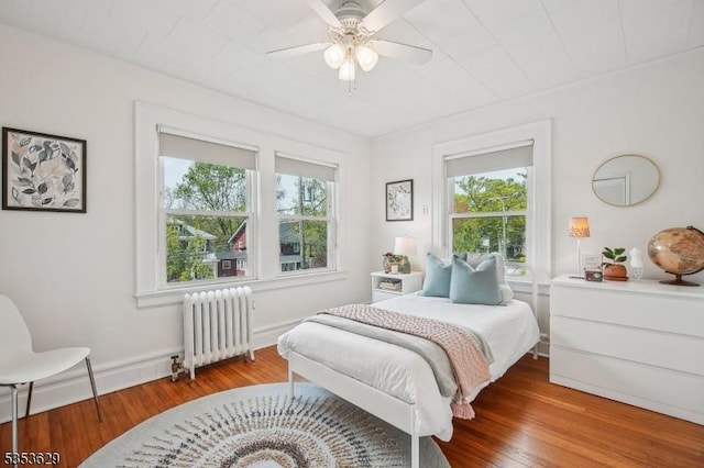 bedroom with radiator heating unit, baseboards, ceiling fan, and wood finished floors