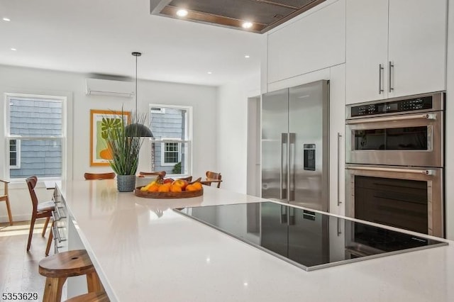 kitchen featuring a wall mounted air conditioner, modern cabinets, a breakfast bar area, white cabinets, and appliances with stainless steel finishes