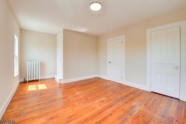 empty room featuring a wealth of natural light, radiator, and light wood-type flooring