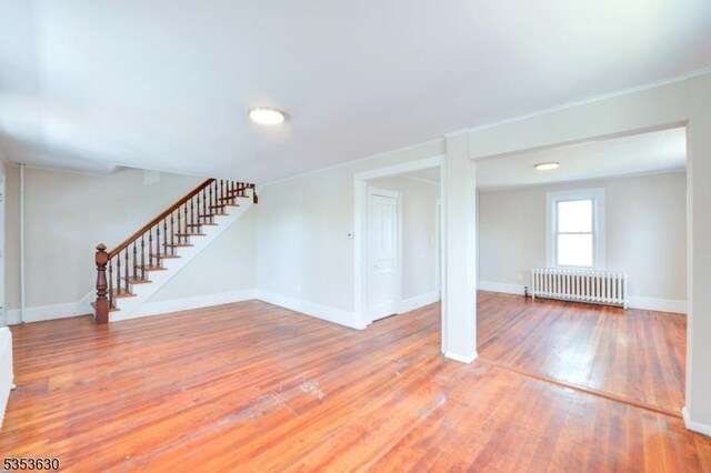 below grade area with baseboards, light wood-style flooring, radiator, and stairs