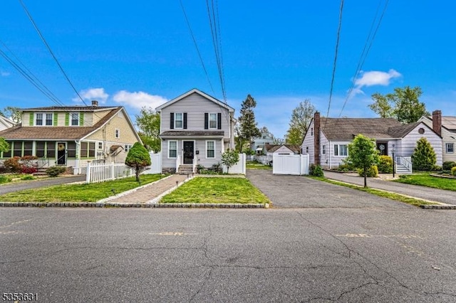 view of front of home with fence, a gate, aphalt driveway, and a front lawn