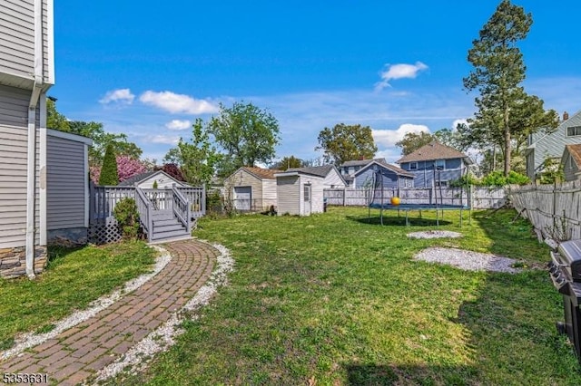 view of yard featuring an outdoor structure, a trampoline, a deck, a storage shed, and a fenced backyard