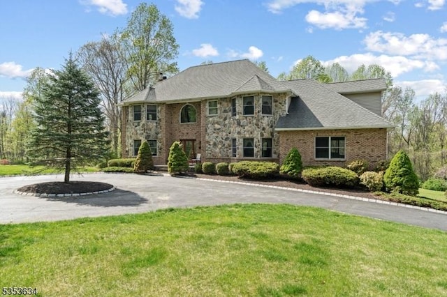 view of front facade featuring curved driveway, a front lawn, stone siding, and brick siding
