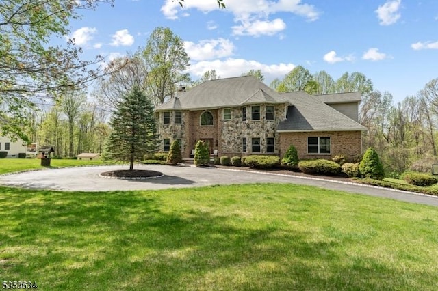 view of front of house with curved driveway, brick siding, and a front yard