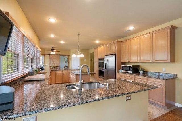 kitchen with a peninsula, recessed lighting, dark stone counters, a sink, and stainless steel appliances
