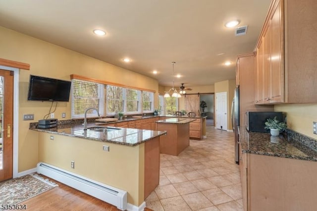 kitchen featuring visible vents, a baseboard radiator, freestanding refrigerator, a peninsula, and dark stone countertops