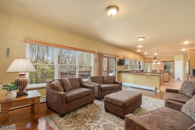 living area with light wood-style floors, a baseboard radiator, and ceiling fan