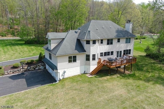 rear view of house featuring a chimney, a deck, a view of trees, a shingled roof, and stairs