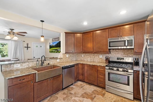 kitchen featuring appliances with stainless steel finishes, a sink, brown cabinetry, a peninsula, and backsplash