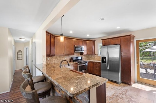 kitchen featuring a peninsula, appliances with stainless steel finishes, light stone counters, and tasteful backsplash