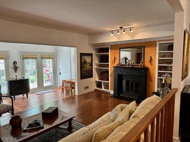 living room featuring a fireplace with flush hearth, built in shelves, crown molding, french doors, and wood finished floors