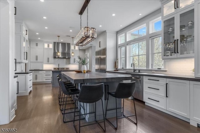 kitchen with backsplash, dark countertops, appliances with stainless steel finishes, a center island, and wall chimney exhaust hood