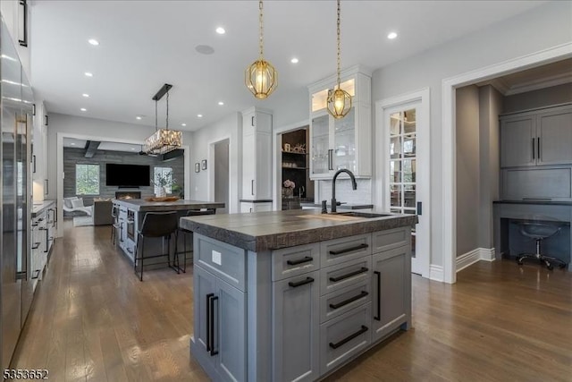 kitchen with gray cabinets, a sink, open floor plan, butcher block countertops, and an island with sink