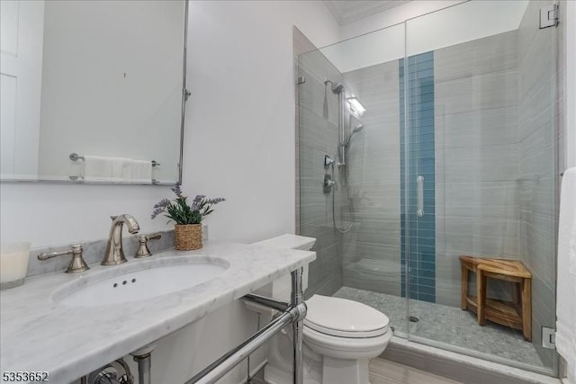 bathroom with a sink, ornamental molding, a shower stall, and toilet