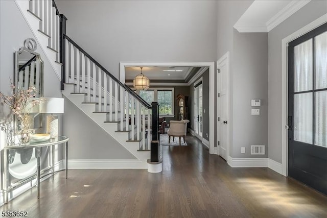 foyer featuring crown molding, visible vents, wood finished floors, baseboards, and stairway