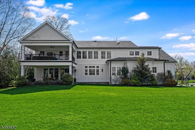 rear view of house featuring a lawn, a ceiling fan, board and batten siding, and a balcony