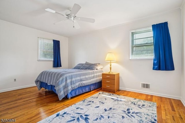 bedroom featuring a ceiling fan, baseboards, visible vents, and wood finished floors