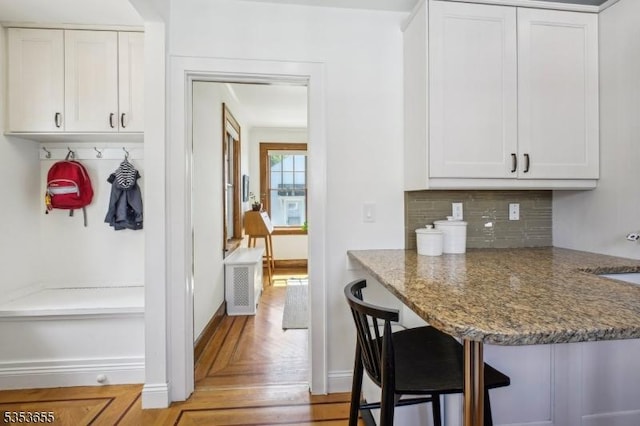 kitchen with a kitchen bar, white cabinets, stone counters, tasteful backsplash, and baseboards
