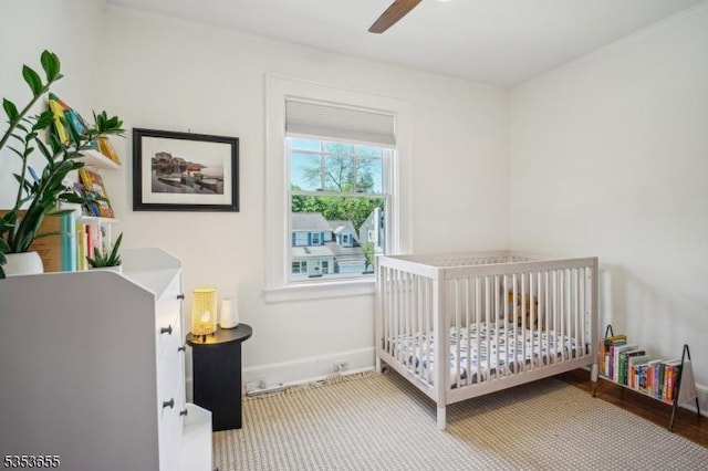 bedroom featuring a nursery area, ceiling fan, and baseboards