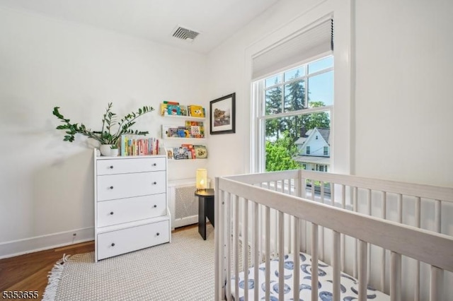 bedroom with a nursery area, wood finished floors, and baseboards