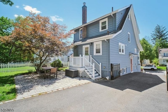 rear view of house featuring fence, a chimney, and a patio