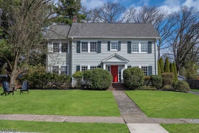 colonial-style house featuring a front lawn and a chimney