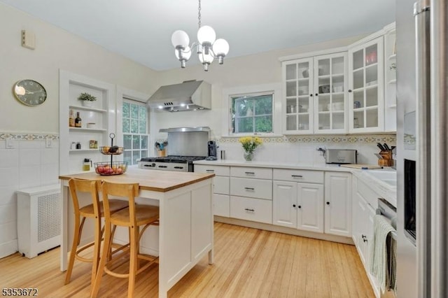 kitchen featuring wall chimney range hood, refrigerator with ice dispenser, stove, white cabinets, and light wood finished floors
