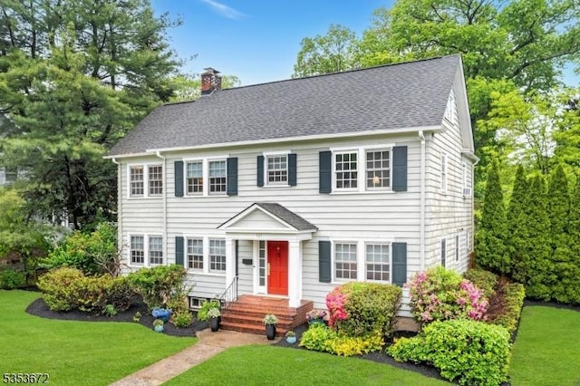 colonial inspired home with a chimney, a front yard, and a shingled roof