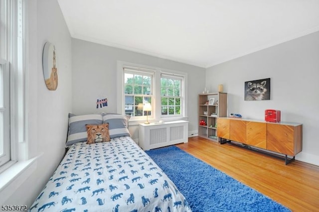bedroom with radiator, wood finished floors, ornamental molding, and baseboards