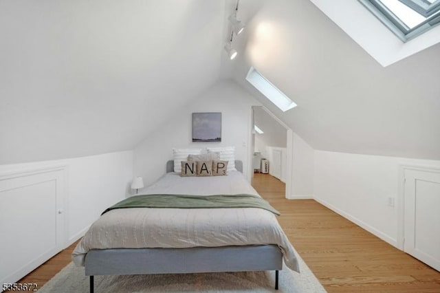 bedroom with a skylight, rail lighting, wood finished floors, lofted ceiling, and baseboards