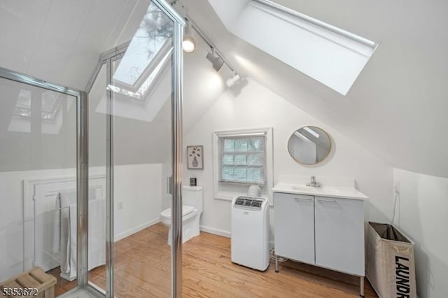 full bathroom with a skylight, vaulted ceiling, wood finished floors, a stall shower, and track lighting