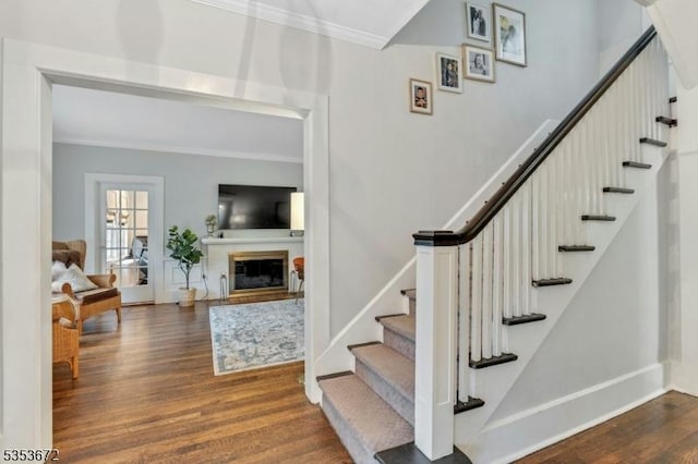 stairs with crown molding, wood finished floors, baseboards, and a glass covered fireplace