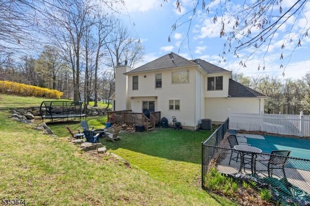 back of house featuring a wooden deck, cooling unit, a fenced backyard, a lawn, and a trampoline
