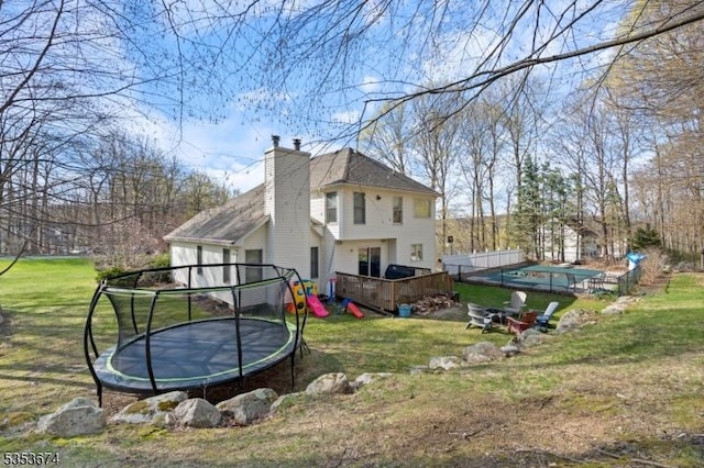 rear view of property with a lawn, a trampoline, a chimney, and a wooden deck