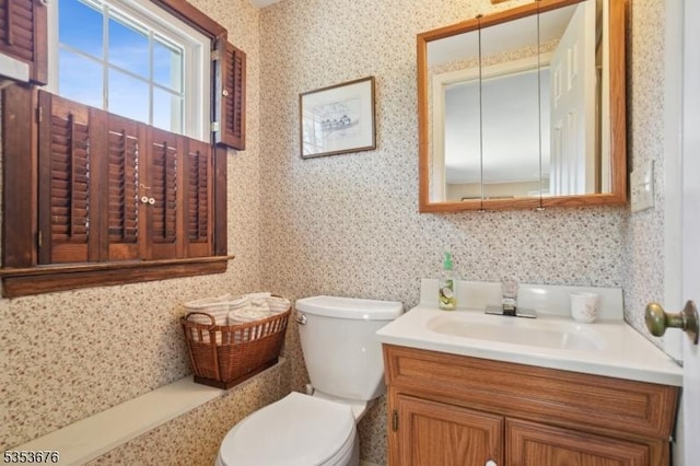 half bath featuring vanity, wallpapered walls, and toilet