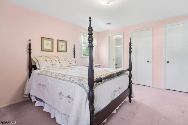 carpeted bedroom featuring visible vents, baseboards, and ensuite bathroom