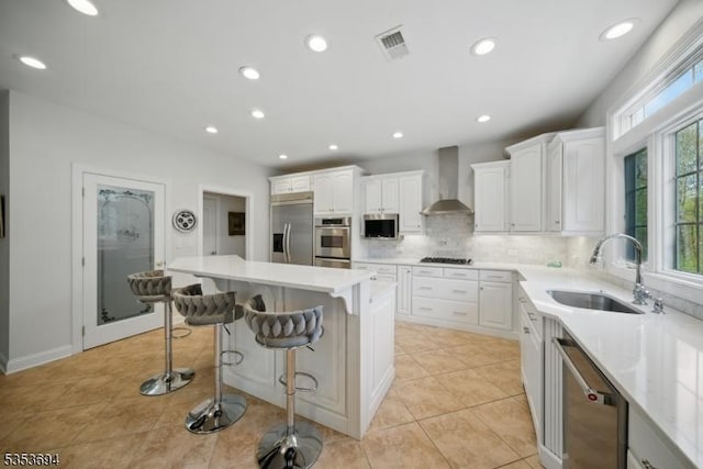 kitchen featuring a kitchen breakfast bar, visible vents, a sink, stainless steel appliances, and wall chimney exhaust hood